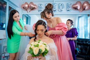 Wedding preparation scene with attendants in bright dresses helping style the bride.