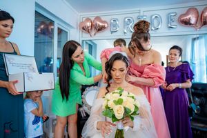 Bridal party in colorful dresses assists during pre-wedding preparations with rose bouquet.