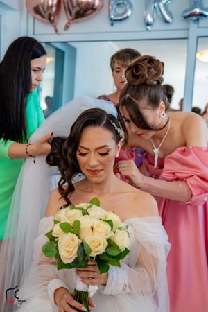 Intimate wedding preparation moment with cream roses and attendants in colorful dresses.