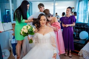Wedding party members in pink and green dresses gather in a bright blue-walled room with decorative balloons.