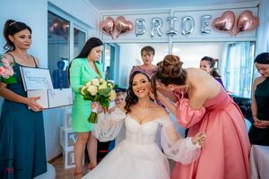 Wedding party celebrates in a bright room with pink balloons and 'BRIDE' wall decorations.