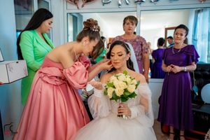 Wedding party gathers around in vibrant dresses of green, pink, and purple during pre-ceremony preparations.