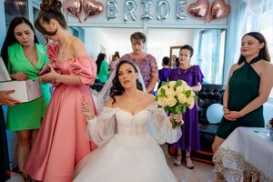 Bridal preparation scene with attendants in colorful dresses under silver balloon decorations.