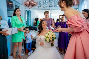 Wedding party surrounds bride in white gown during pre-ceremony preparations.