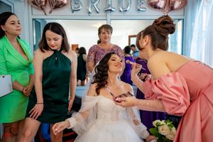 Final touches being applied during wedding preparation with bridesmaids in jewel-toned dresses.