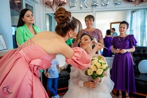 Wedding preparations show a makeup artist in pink applying cosmetics to a bride holding a yellow rose bouquet.