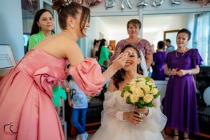 A candid moment shows laughter during bridal makeup application with attendants watching in the background.
