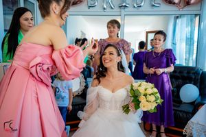 A cheerful wedding preparation scene with a bride getting makeup done while holding a yellow rose bouquet.