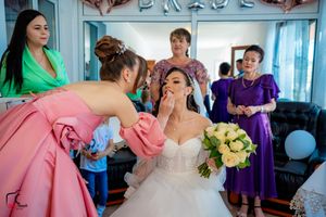 Final wedding preparations show makeup application in progress with attendants in colorful dresses watching.