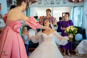 Wedding party members in purple and pink dresses gather in a bright blue-walled room during preparations.