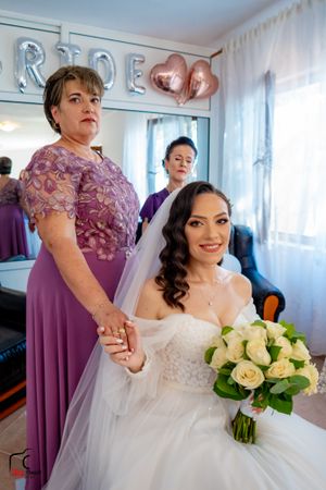 Bride in white gown holds yellow rose bouquet while surrounded by purple-dressed attendants.