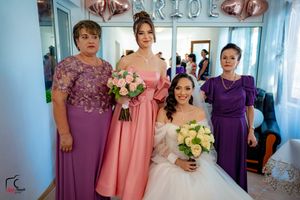 Wedding party members in purple and pink dresses gather for photos in a bright room with blue curtains.