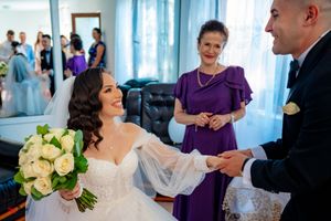 Wedding party members in formal attire gather in a room with blue drapes and natural light.