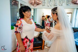 Wedding party members share joyful moments in a bright room with mirrors and floral dresses.