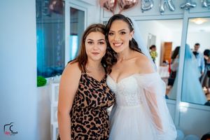 Wedding party members in formal attire gather for photos in a bright indoor venue with blue walls.