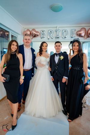 Wedding party members in black and white formal attire pose together indoors.