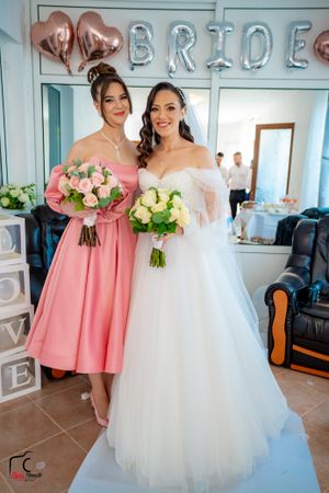 Bridesmaids in coral pink dresses hold bouquets next to bride in white gown.