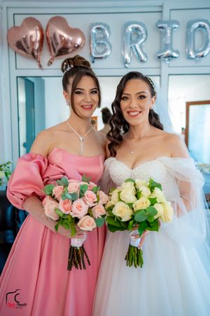 Wedding party members hold pink and cream rose bouquets against light blue walls.