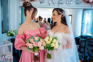 Wedding party members hold beautiful bouquets of pink and white roses in a blue-tinted room.