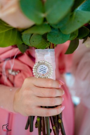 Close-up of hands holding a bouquet with an ornate pearl-rimmed tag detail.
