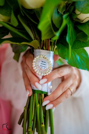 White manicured hands holding a floral bouquet with a decorative pearl-framed tag.