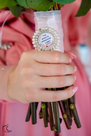 Detailed shot of hands holding flower stems with an ornate circular pearl embellishment.