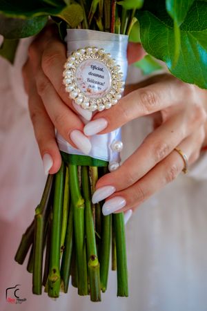 Elegant white manicured nails holding a bouquet wrapped with a pearl-decorated tag.