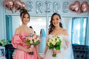 Bridal party posing under rose gold balloon decorations in a blue-tinted room.