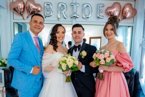 Wedding party members gather in front of 'BRIDE' balloon letters in a decorated indoor space.