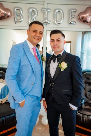 Wedding party members pose in formal attire with balloon decorations and black leather seating.