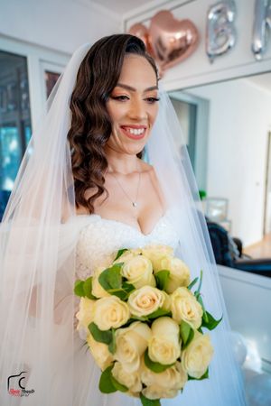 A bride in a white wedding dress holds a bouquet of cream roses while smiling radiantly on her special day.