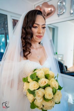 A bride wearing a delicate veil holds a beautiful bouquet of cream roses against a light background.