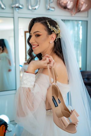 Bride in off-shoulder gown shows off nude heels while wearing crystal hair accessory and veil.