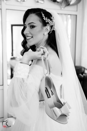 Black and white portrait of bride holding shoes, featuring elegant hair accessory and flowing veil.