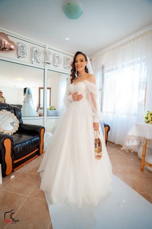 Full-length shot of bride in flowing white gown standing in front of silver balloon letters.