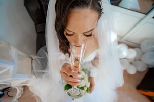 Bride in white veil sips from a champagne flute while getting ready on her wedding day.