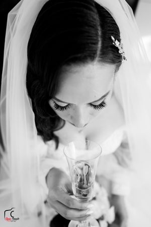 A close-up black and white photo of a bride in a veil looking down at her champagne glass.