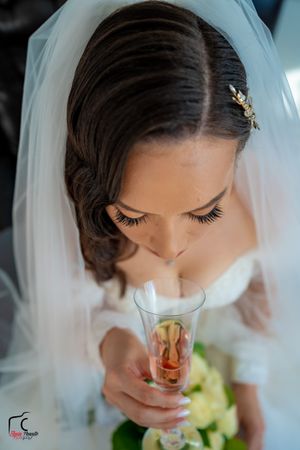 Overhead view of a bride in a white veil drinking from a decorated champagne glass.