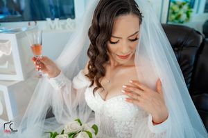 Joyful bride in lace dress holds champagne while touching her heart on her wedding day.