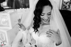 Black and white photo of a happy bride holding champagne and touching her heart.