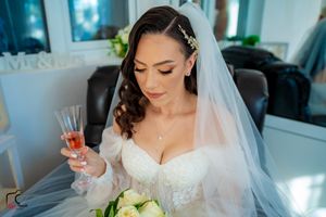 Elegant bride in lace dress holds champagne while seated in a leather chair.