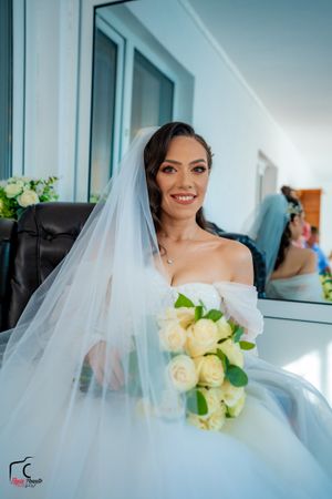 Bride holding cream rose bouquet in natural window light with flowing veil.