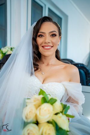Bride with elegant makeup holding pale yellow rose bouquet against light background.