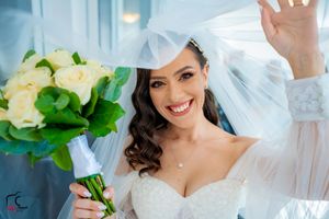 A bride in a white wedding dress holds a bouquet of cream roses under a flowing veil.