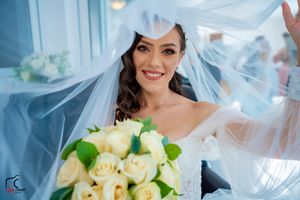 Ethereal bridal portrait with flowing veil and cream roses against light blue background.