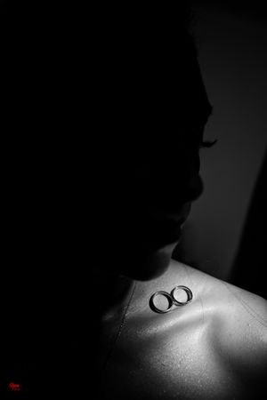 Two wedding rings photographed in dramatic black and white lighting on bare skin.