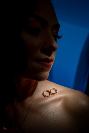 Wedding rings placed on skin with dramatic lighting against deep blue background.