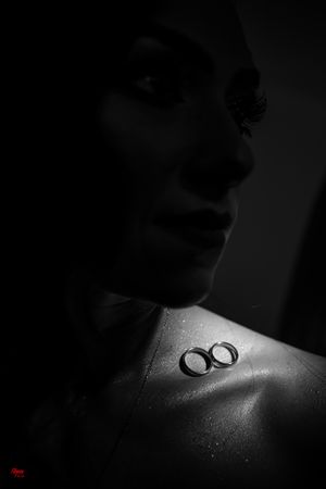 Two wedding rings captured in dark, dramatic lighting on bare shoulder.