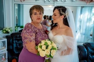A tender moment shared between a bride in white and a woman in purple holding a bouquet of cream roses.