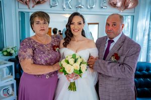 Wedding party poses together in a light blue room with white tulle dress and purple attire.